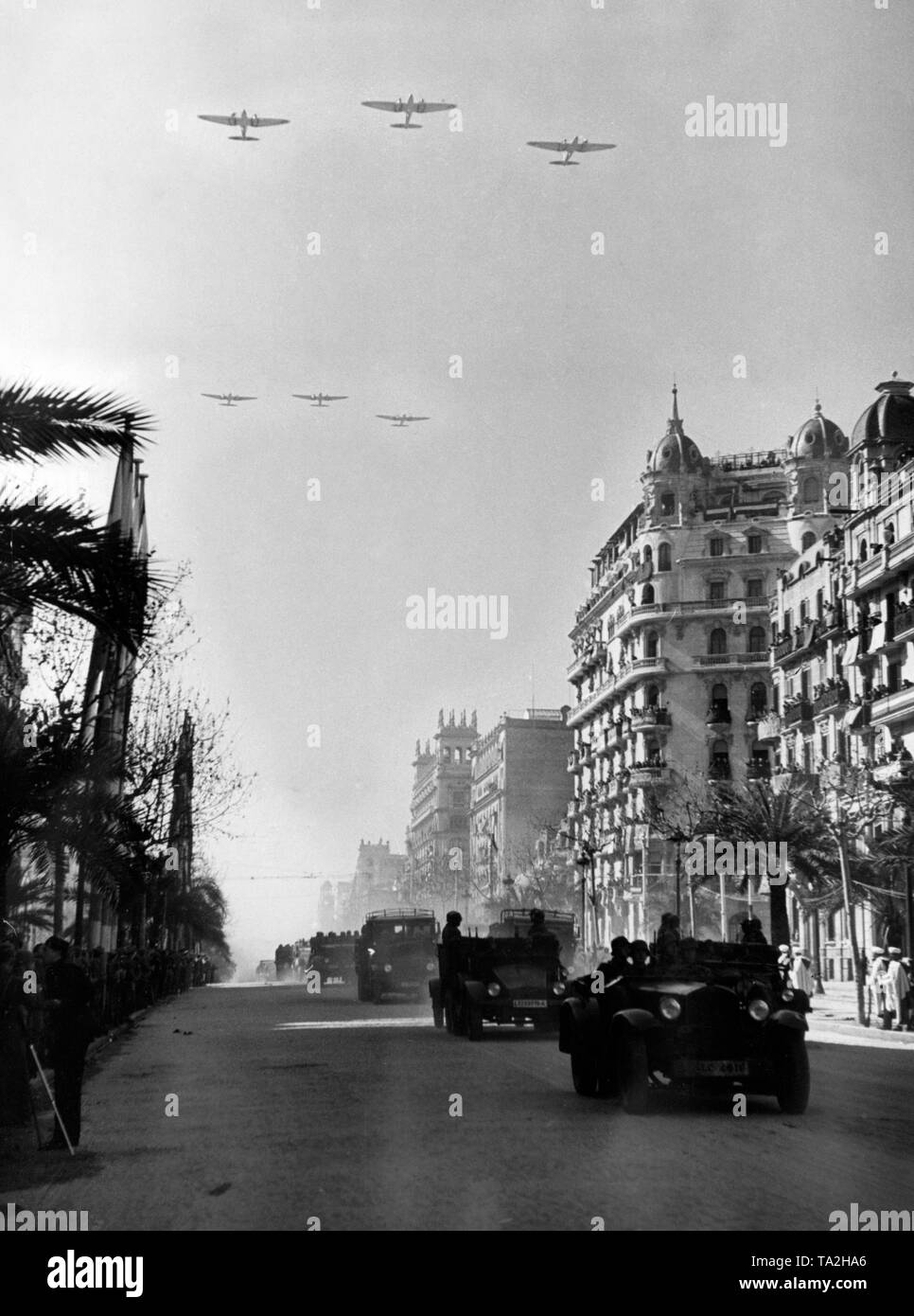 Foto einer Siegesparade der spanischen nationalen Einheiten, einschließlich der Legion Condor, auf dem Passeig de Colon nach der Eroberung (Januar 1939) von Barcelona, die von General Francisco Franco am 21 Februar, 1939. Zwei deutsche Traktoren, Typ Krupp L2H143, sind auf der Straße. Im Himmel, drei Heinkel He 111 Bomber im Formationsflug. Stockfoto