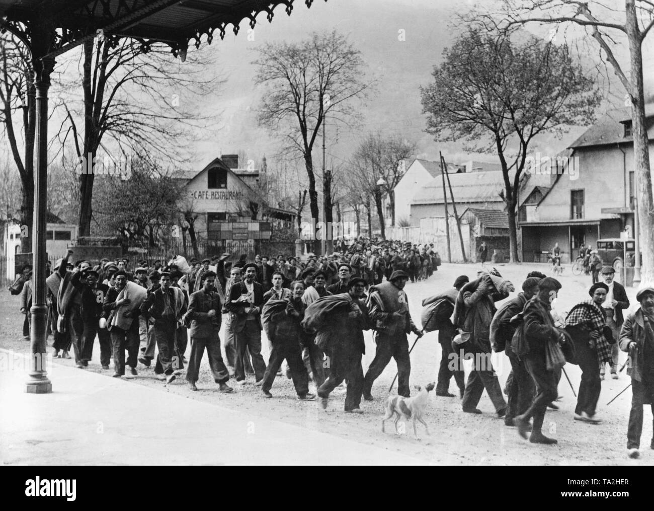 Foto einer Spalte mit ehemaliger Flüchtling republikanischen Soldaten auf dem Bahnhofsplatz in den Französischen Pyrenees-Bagneres-de-Luchon direkt hinter der französisch-spanischen Grenze. Die Männer tragen Decken, tragen ihr Gepäck, und sind bereits unscharfgeschaltet ist. Sie werden von den Einwohnern von Luchon beobachtet. Foto von April, 1938. Stockfoto