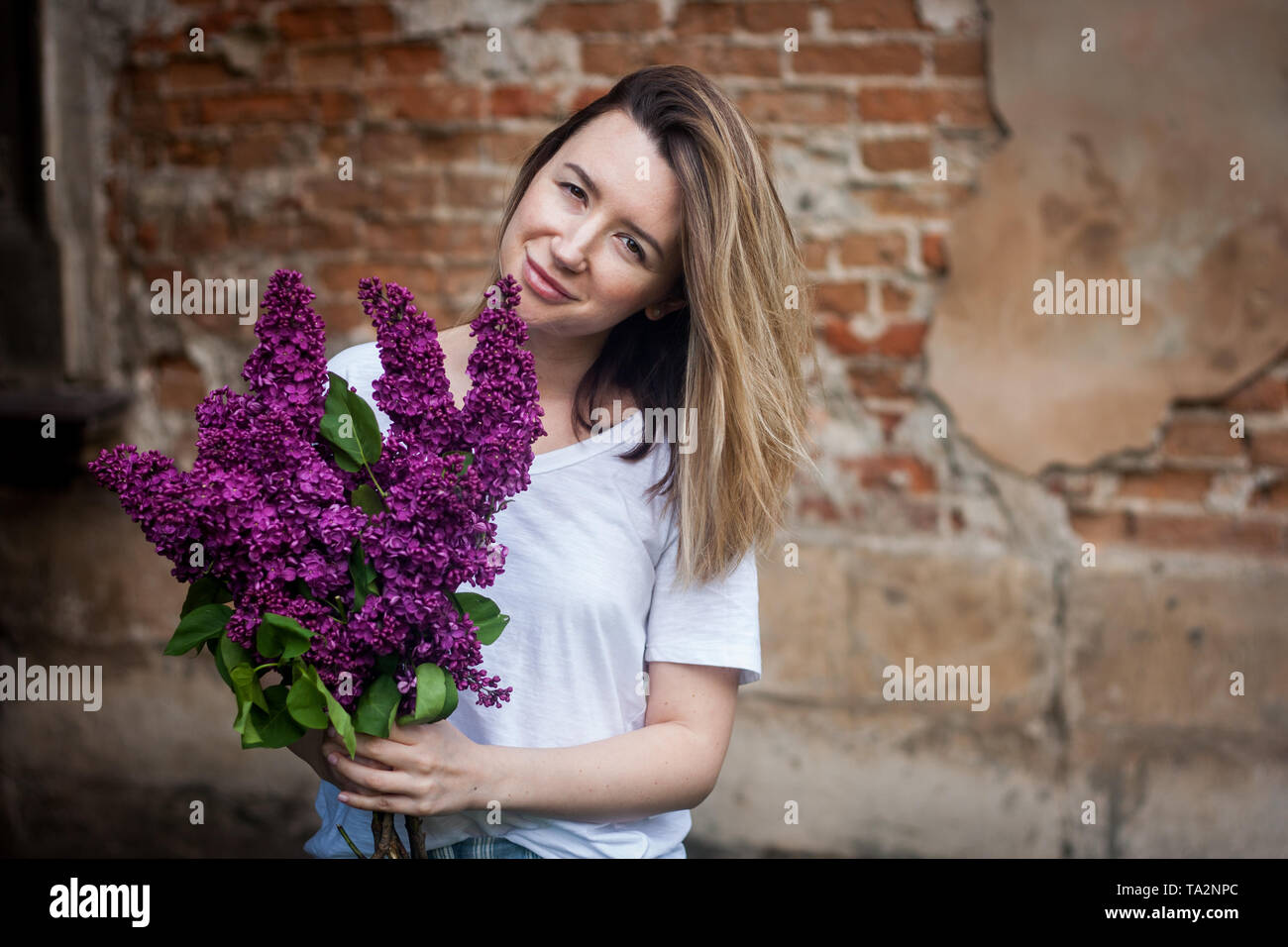 Stilvolle Frau, die eine lebendige Haufen lila Blüten. Grunge Red brick wall Hintergrund. Stockfoto