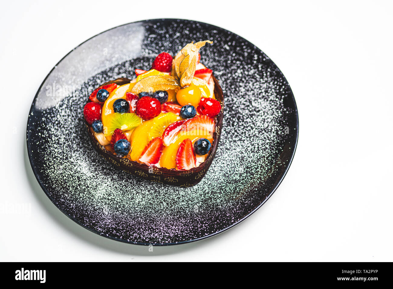 Herzförmige Frucht Biskuitteig, Obstkuchen auf schwarze Platte bestreut mit Puderzucker. Gesunde Süßwaren Hintergrund. Platz kopieren Stockfoto