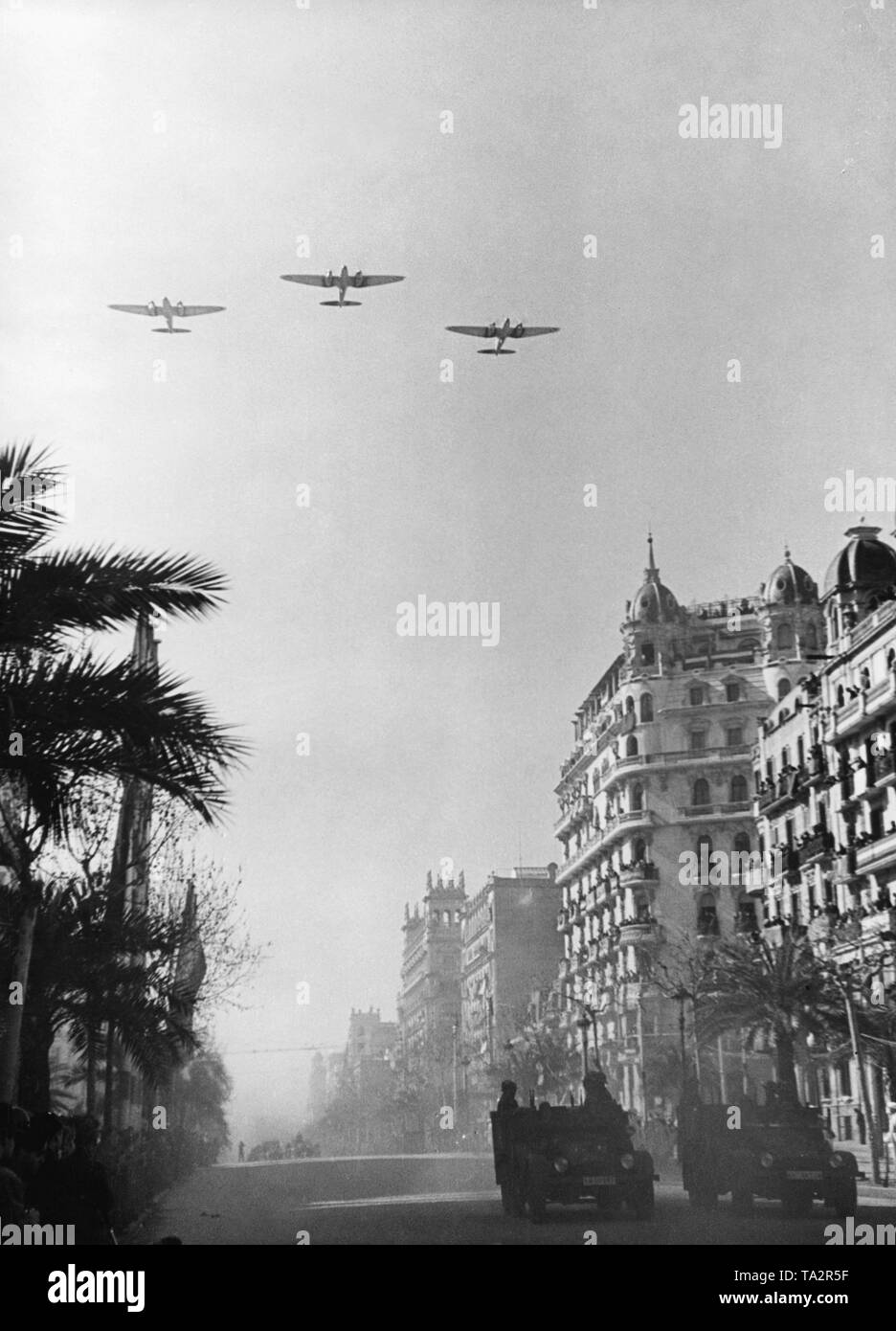 Foto einer Siegesparade der spanischen nationalen Einheiten, einschließlich der Legion Condor, auf dem Passeig de Colon nach der Eroberung (Januar 1939) von Barcelona, die von General Francisco Franco am 21 Februar, 1939. Zwei deutsche Traktoren, Typ Krupp L2H143, sind auf der Straße. Im Himmel, drei Heinkel He 111 Bomber im Formationsflug. Stockfoto