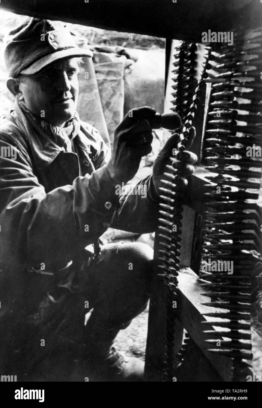 Ein MG-Schütze reinigt die bandolier mit Sand in einem Tierheim gefüllt mit seinem rasierpinsel. Stockfoto