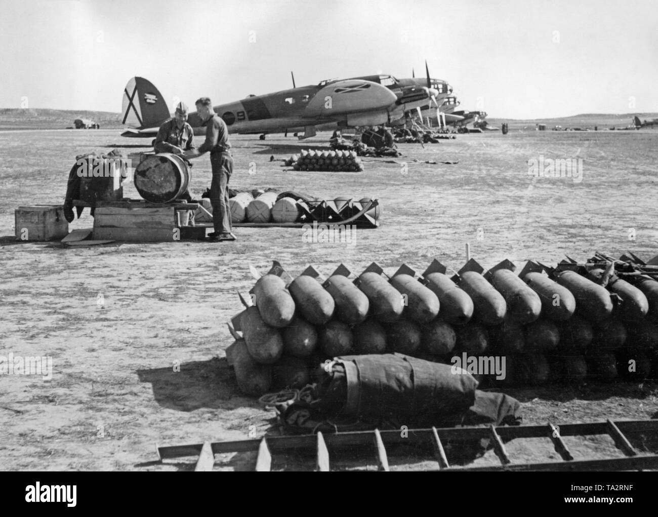 Foto der deutschen Heinkel He 111 Fighter Bomber der Legion Condor (Bomber Gruppe K/88) auf dem Flugplatz von Lérida, Katalonien, 1939. Im Vordergrund Es gibt Granaten. Hinter, Personal am Boden arbeiten. Die Saint Andrew's Cross der Spanischen Luftwaffe ist auf der vertikalen Schwanz sichtbar. Stockfoto
