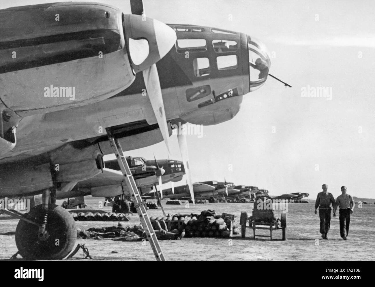 Foto der deutschen Heinkel He 111 Fighter Bomber der Legion Condor (Gruppe Combat 88) auf dem Flugplatz von Lérida, Katalonien, 1939. Vor der Bomber Es gibt Granaten. Zwei Offiziere des Bodenpersonals sind zu Fuß neben Ihnen. Dargestellt, die vorwärts gunner Fach, das aus Plexiglas mit integriertem Maschinengewehr für die Verteidigung von Kampfflugzeugen gemacht wurde. Stockfoto