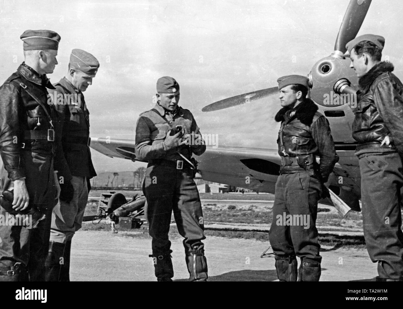 Foto von vier jungen Offizieren der Fliegertruppe (Air Force Truppe) der Legion Condor im Gespräch mit Kapitän (Mitte) vor einem deutschen Kampfflugzeuge vom Typ Messerschmitt Bf 109 B, auf einem Flugplatz in Spanien. Hier der Fang des Maschinengewehr in die Mulde der Propeller in die Nase. Stockfoto