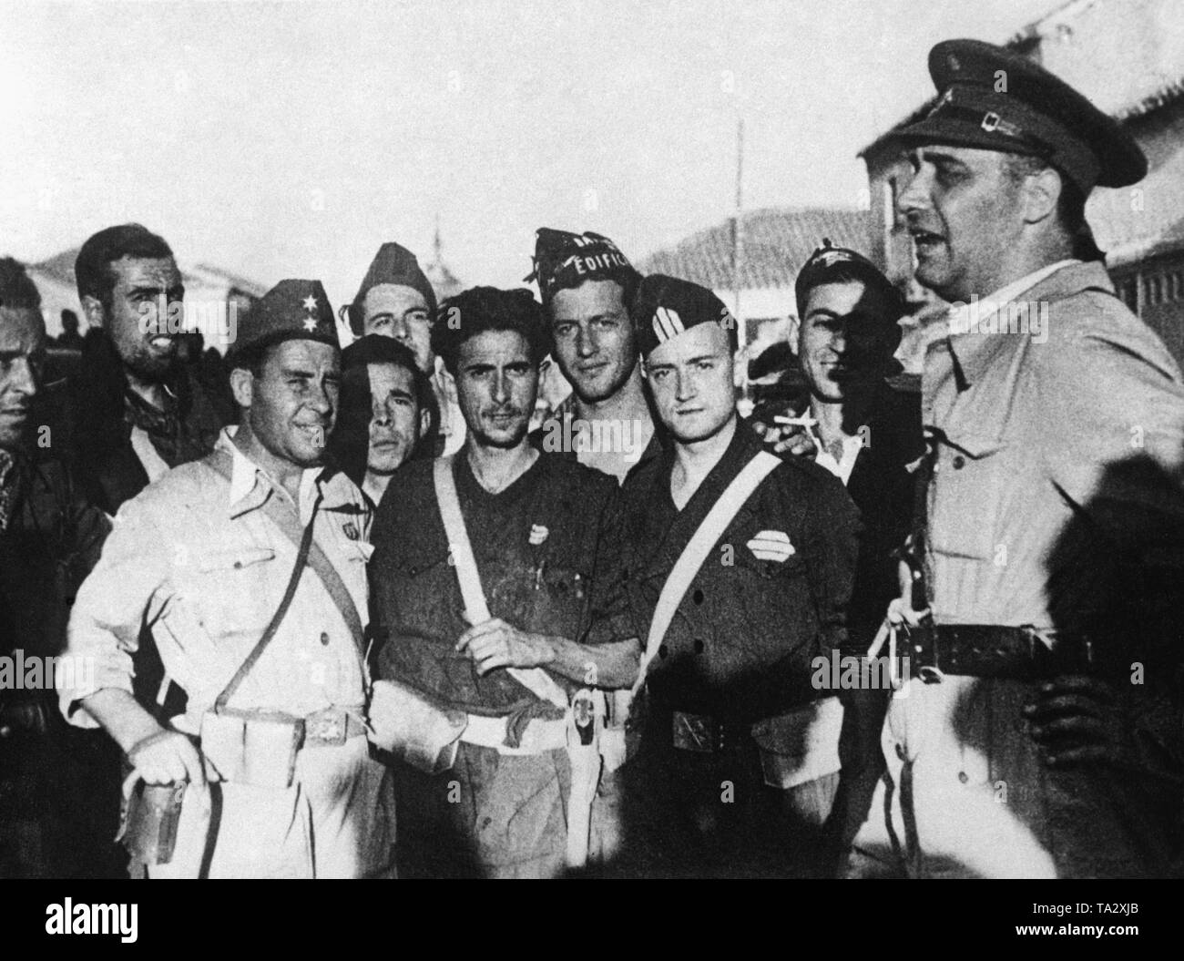 Foto von einer Gruppe von Soldaten im Gespräch mit dem republikanischen Kriegsminister, General Jose Asensio Torrado (ganz rechts mit Regenschirm) in Toledo. Dritter von links, im hellen Bereich Tunika, ein TENIENTE (Offizier, Lieutenant), dritter von rechts, ein SARGENTO (sergeant). Stockfoto