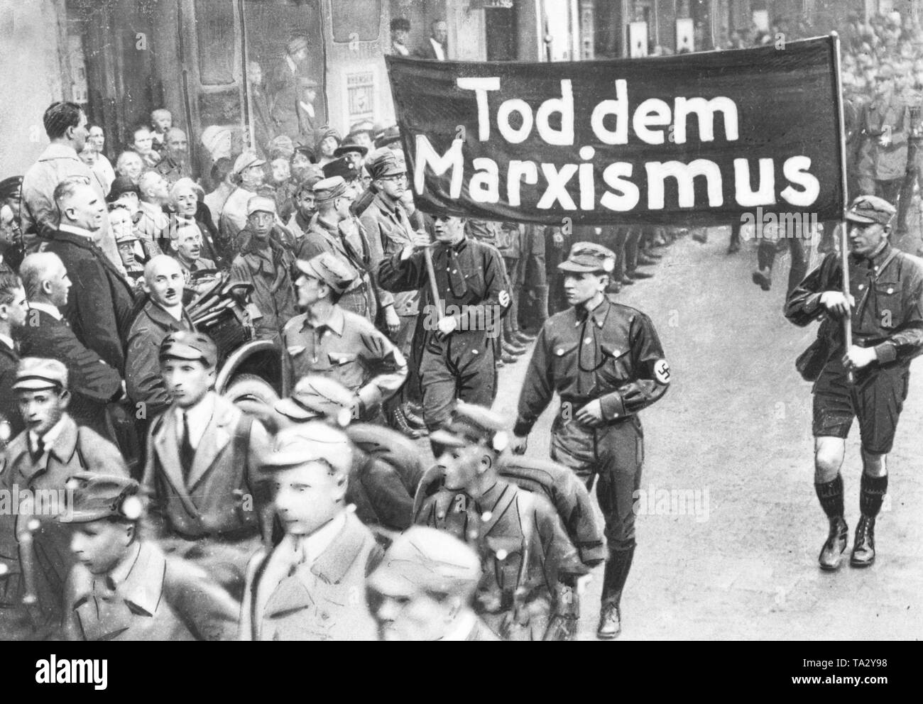 Adolf Hitler (links stehend im Hellen dustcoat) am März Vergangenheit der SA während der Parteitag der NSDAP in Weimar. Unter ihm auf der rechten Seite ist der Herausgeber der "tuermer" Julius Streicher. Zwei SA-Männer halten ein Transparent mit der Aufschrift "Tod des Marxismus". Stockfoto
