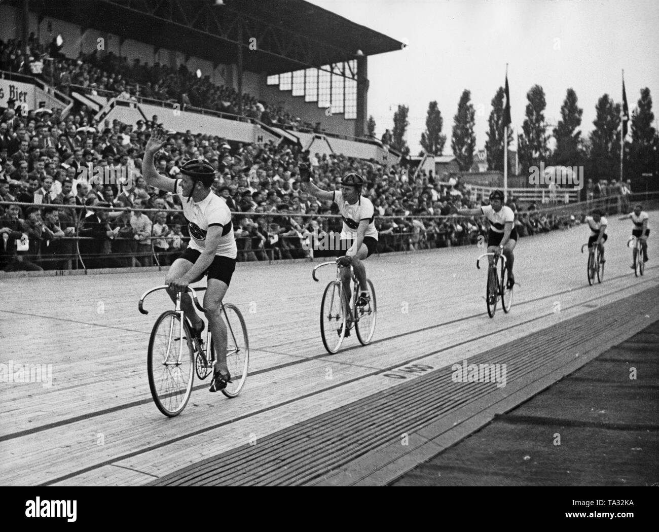 Die deutschen Bahnradfahrer wave für die Zuschauer auf der ersten Fahrt auf dem Olympiaradrennbahn in Berlin am 25. Juli 1936. Stockfoto