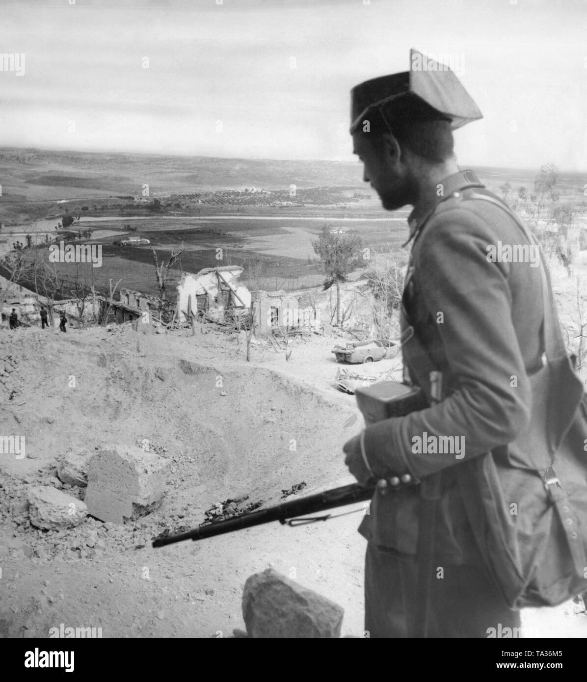 Foto der Guardia Civil Soldat (paramilitärische Polizeieinheit, die meist die französischen Truppen im Spanischen Bürgerkrieg verbunden), blickt zurück auf den Ruinen der Alcazar von Toledo (Toledo Festung). Im Hintergrund, die Landschaft. In der Mitte, Soldaten sind durch die Shell Krater. Stockfoto