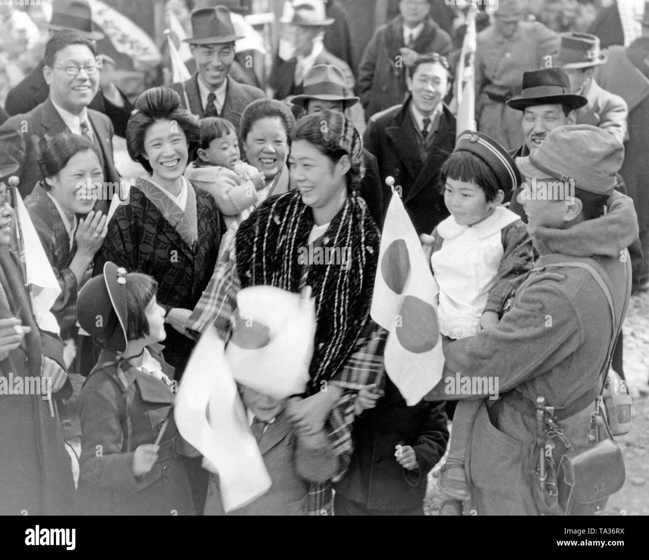 Eine Gruppe von Menschen nehmen Abschied von einem japanischen Soldaten, der in China an der Vorderseite während des Zweiten Japanese-Chinese Krieg geschickt wird. Sie halten japanische Flaggen in den Händen und Lachen. Stockfoto