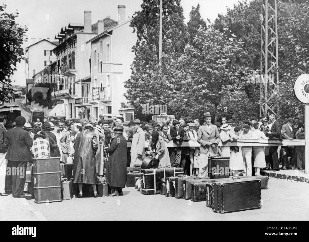 Nach dem Ausbruch des Bürgerkriegs in Spanien im Juni 1936, eine Gruppe von spanischen Flüchtlinge aus dem spanischen Baskenland warten auf die Möglichkeit der sicheren Frankreich an der Irun eintragen Überfahrt nach Hendaye (eine Brücke), an der französischen Atlantikküste am 22 Juni, 1936. Im Vordergrund, Koffer. Im Hintergrund, das Zeichen der Hendaye, rechts das Ortsschild von Hendaye, der den Eintrag in die Französische Zollgebiet. Kurz bevor das Foto gemacht wurde, die spanische Stadt San Sebastian (24 Km westlich) in die Hände der Spanischen Truppen gefallen war. Stockfoto