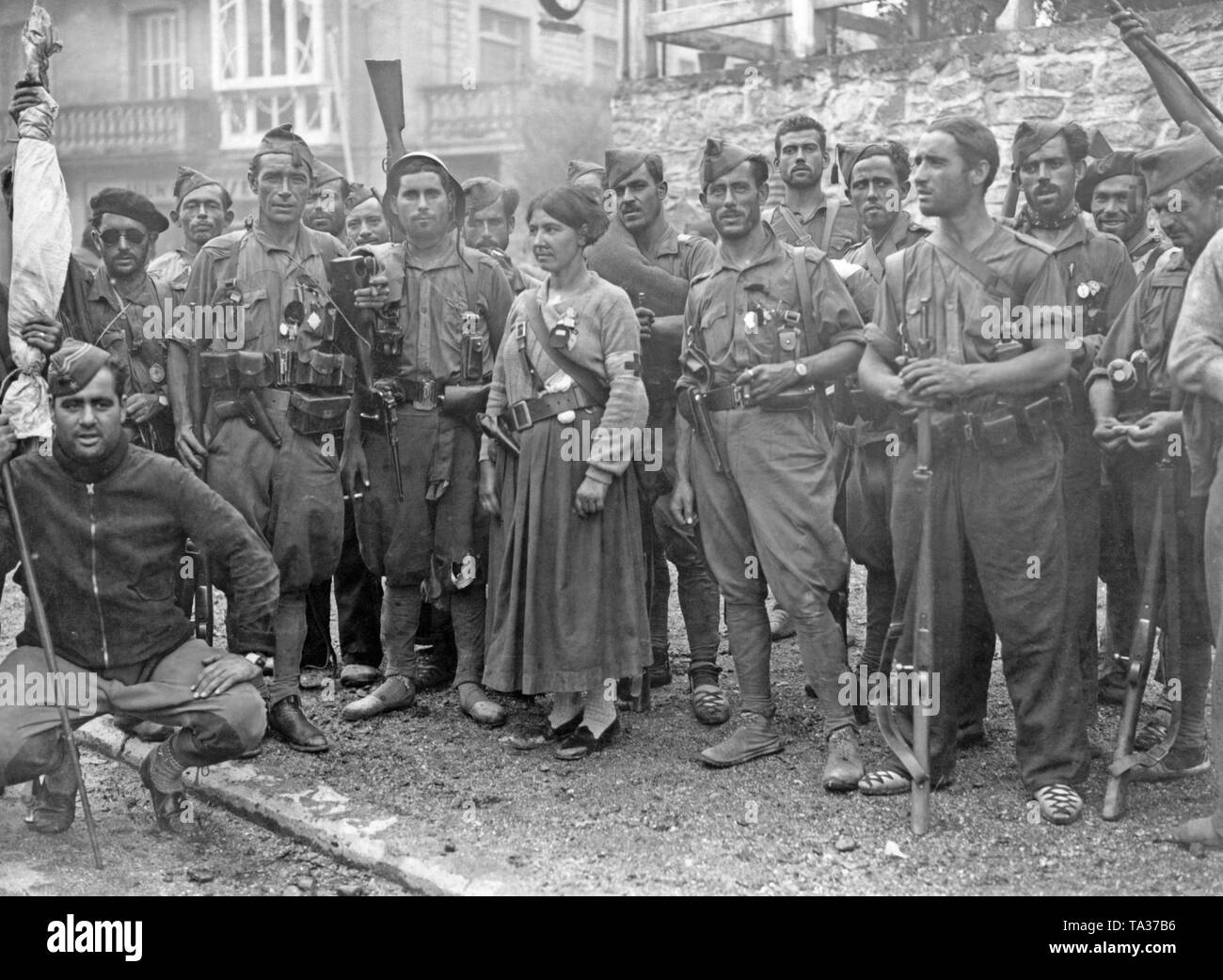 Foto von einer Gruppe von Kämpfern auf der Seite der Regierungstruppen in der Baskischen Grenzstadt Irun (Frankreich), vermutlich im Sommer 1936. Die Kämpfer tragen verschiedene einheitliche Stücke (Latzhosen und Feld tuniken) bzw. sind teilweise in Zivilkleidung. Sie sind mit leichten Waffen, insbesondere Karabiner und Revolver bewaffnet. Auf der linken Seite, ein Teniente (Leutnant), wahrscheinlich der Kommandeur der Einheit, ruht auf einem Stock. In der Mitte stellt ein Medic mit einem roten Kreuz Armband. Sie ist mit einem Revolver bewaffnet. Einige Soldaten tragen alpargatas, einfache Baumwolle Schuhe mit geflochtenem Hanf Sohlen. Stockfoto