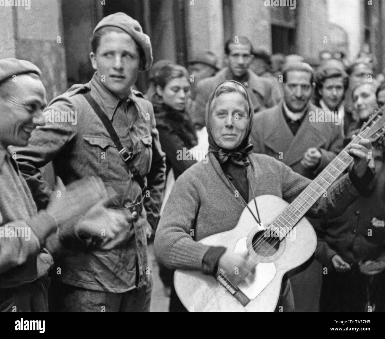 Foto einer Frau spielt die Gitarre für republikanische Soldaten in einer unbekannten Stadt während des Spanischen Bürgerkriegs. Stockfoto
