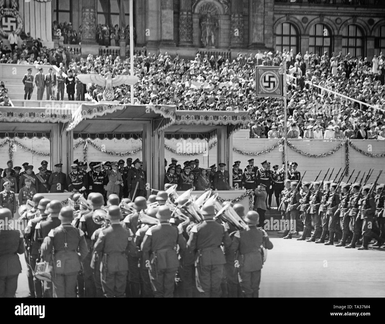 Foto der VIP-Messestand während der Parade für die Legion Condor auf der Ost-West-Achse (ehemalige Chalottenburger Chaussee, heute Straße des 17. Juni) vor der Hauptfassade der Technischen Universität in Berlin am 6. Juni 1939. Adolf Hitler (unter einem Vordach) ist die marschierenden Soldaten den Hitlergruß. Unter der Reichsadler (Imperial Eagle) mit einem Hakenkreuz, ein Radio Kommentator links. Die Musik Band der Wehrmacht spielt. Stockfoto