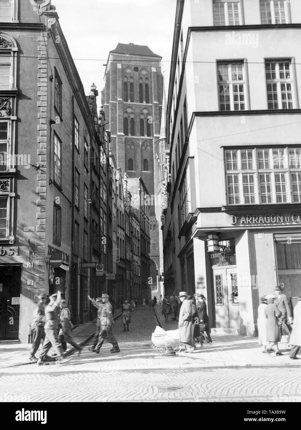 Deutsche Besetzung Soldaten patrouillieren durch Danzig und grüßen mit Hitlergruss, im Hintergrund der Turm der St. Mary's Kirche. Stockfoto
