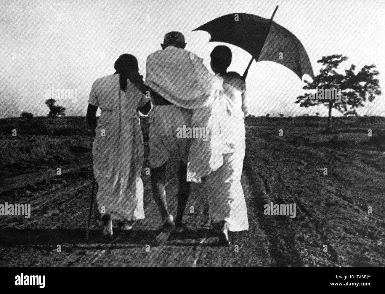 Der Führer der indischen Unabhängigkeitsbewegung Mahatma Gandhi wird durch zwei junge Mädchen auf seinem Weg unterstützt. Stockfoto