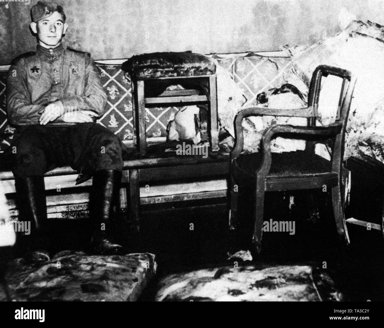 Foto von einem sowjetischen Soldaten durch einen amerikanischen im Fuehrerbunker', kurz nach der Übernahme der Reichskanzlei von sowjetischen Truppen eingenommen. Der Soldat trägt die Reihenfolge der Red Star (militärische Dekoration) auf seinem rechten Brust, und sitzt auf dem Sofa im Zimmer, wo Hitler und Eva Braun ihr Leben nahm. Stockfoto