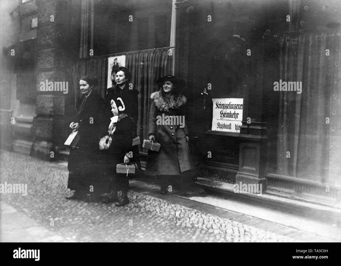 Drei Frauen und ein Mädchen stehen vor einem Büro mit der Inschrift "Kriegsgefangene homecoming Informationen hier". Alle drei von ihnen halten Sie ein Geschenk in Ihren Händen, das sie als Angehörige eines Kriegsgefangenen erhalten haben. Stockfoto