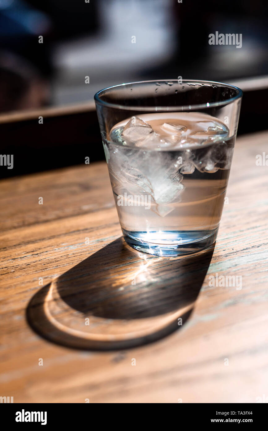 Ein Glas eiskaltes Wasser werfen Ihren Schatten auf eine Holz- Oberfläche. Stockfoto