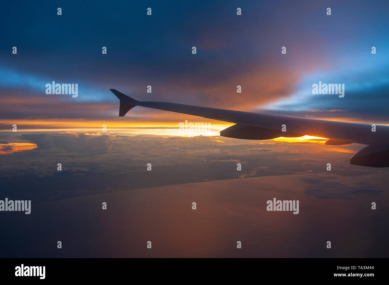 Luftaufnahme durch das Fenster eines Flugzeugs bei Sonnenuntergang mit einem Flugzeugflügel. Konzept der Reise-, Transport- und Langstreckenflüge. Stockfoto