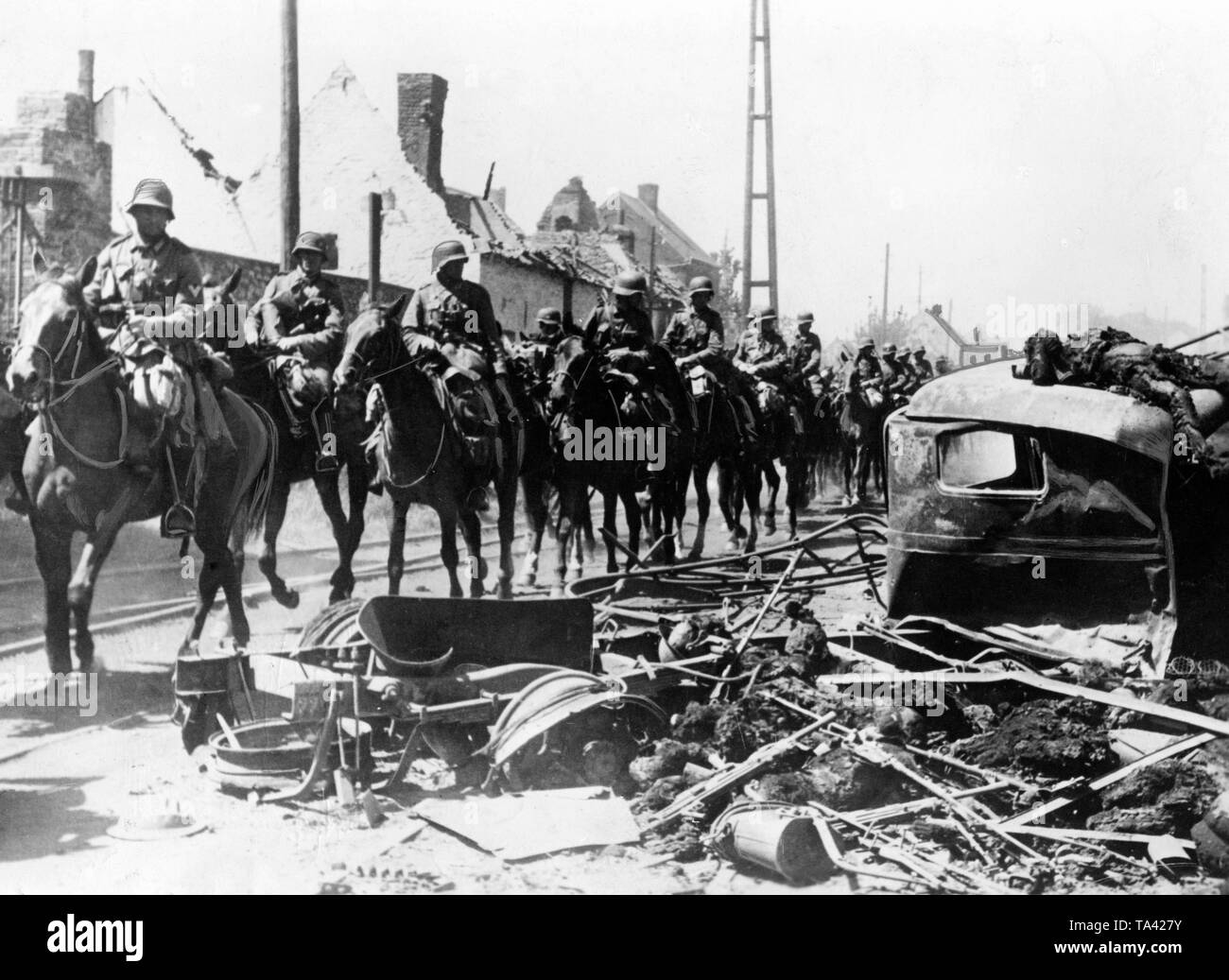 Deutsche Kavalleristen durch ein französisches Dorf, rechts im Bild ein zerstörtes Fahrzeug und die toten Besatzungsmitglieder. Obwohl die westlichen Kampagne mehr mit Panzern verknüpft ist, wird die Wehrmacht setzte auch eine komplette Kavallerie Division. Stockfoto