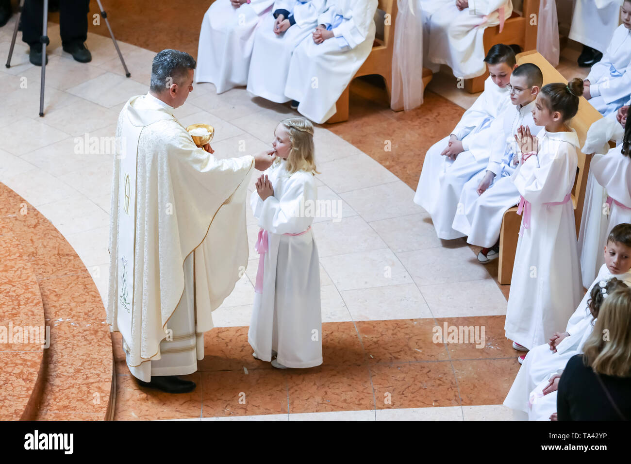 Zagreb, Kroatien - 5. Mai 2019: Der Priester gibt Erstkommunion für die Kinder in weißen Kleidern während der Kommunion in der Kirche von Alle gekleidet Stockfoto