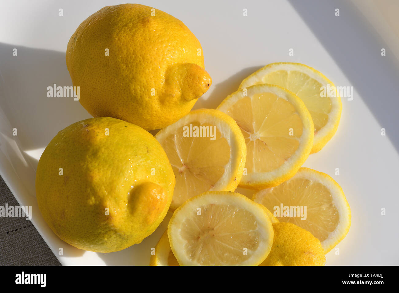 Ganze und aufgeschnittene Zitronen auf weißem Platter Stockfoto