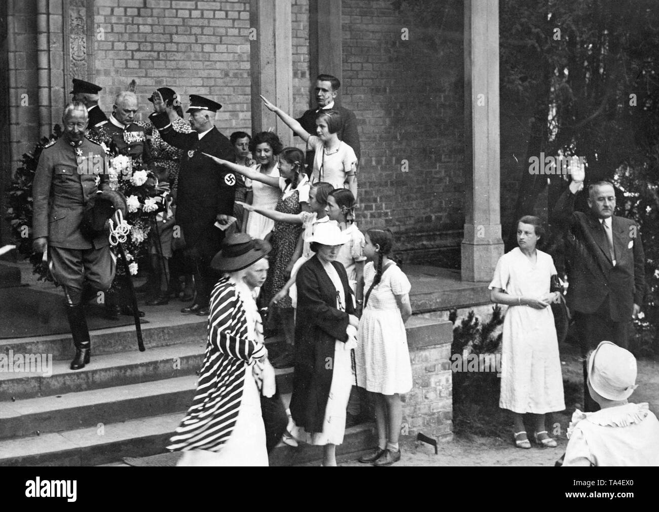 Kronprinz Wilhelm (links) in der husar Uniform, Verlassen der Waldkirche in Nikolskoe (heute ein Stadtteil von Berlin) nach einer Trauerfeier. Er ist mit dem Hitlergruß von einigen Kindern begrüßt. Der Service war durch eine Kranzniederlegung am Grab des Kronprinzen Friedrich Karl gefolgt. Stockfoto