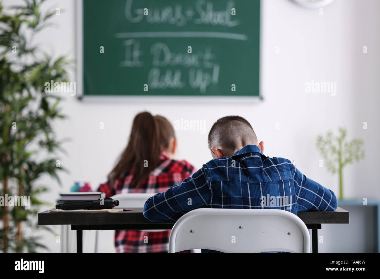 Süße kleine Jungen mit Pistole an den Schreibtisch im Klassenzimmer sitzen. Konzept der Schule schießen Stockfoto