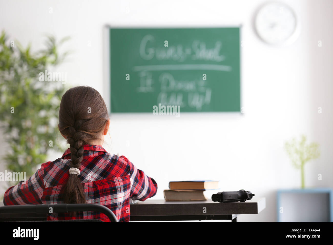 Süße kleine Mädchen mit Pistole an den Schreibtisch im Klassenzimmer sitzen. Konzept der Schule schießen Stockfoto