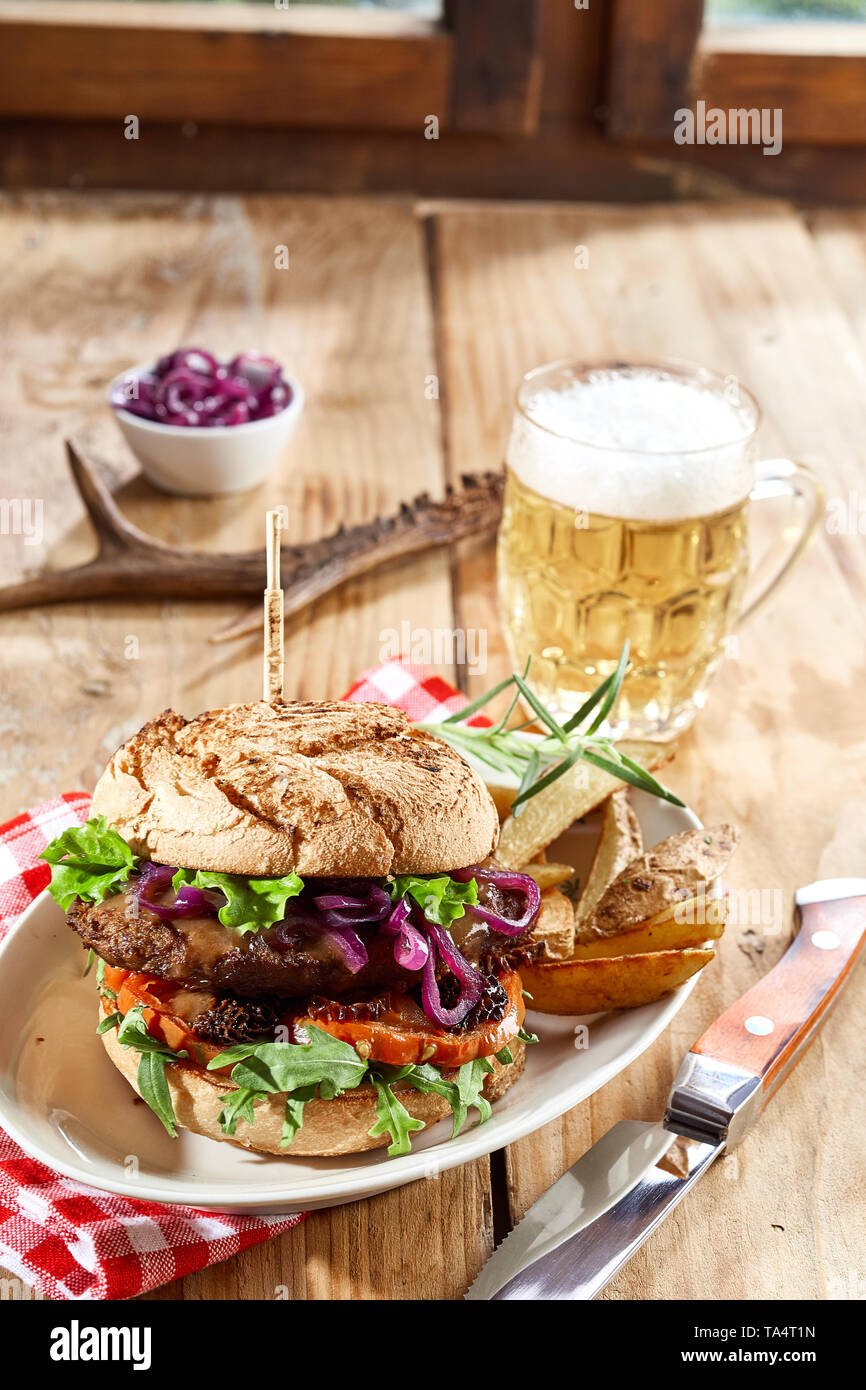 Wild Wild Beef Burger mit Salat Beilagen auf einem Teller mit  Kartoffelecken und eine kalte schaumiges Bier auf einer rustikalen Tisch  serviert, Seitenansicht für Menü Stockfotografie - Alamy