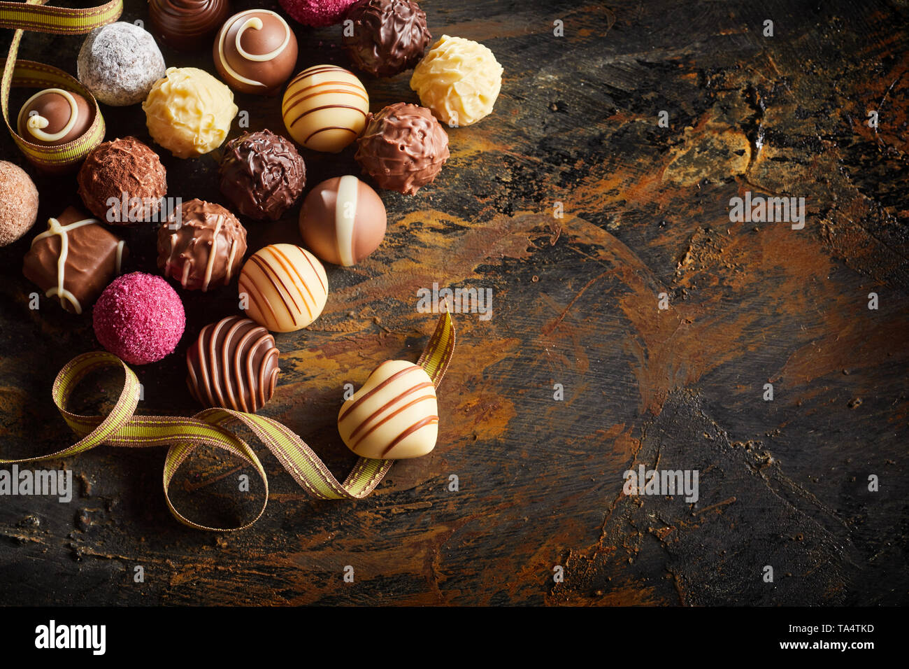 Gourmet Schokolade Valentinstag noch Leben mit einer großen Auswahl an Luxus handgefertigte Pralinen mit einem Herzförmigen Bonbon auf einem Twirled ribbon Sym Stockfoto