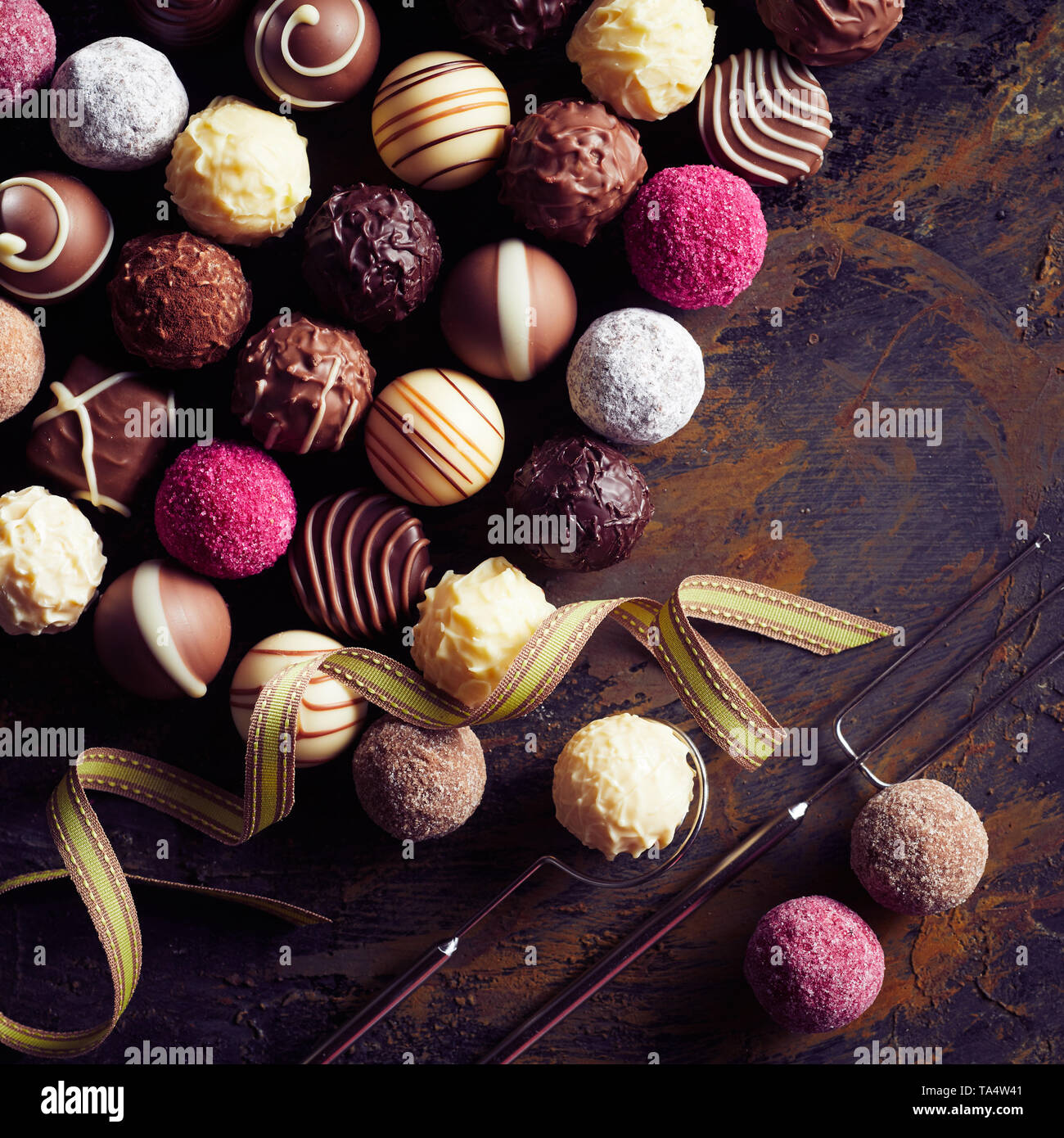 Große Auswahl an Luxus handgemachten Pralinen Schokolade mit dekorativen Kugeln mit einem Kabel Gabel und Heber auf alten Vintage Holz im quadratischen Format angezeigt. Stockfoto