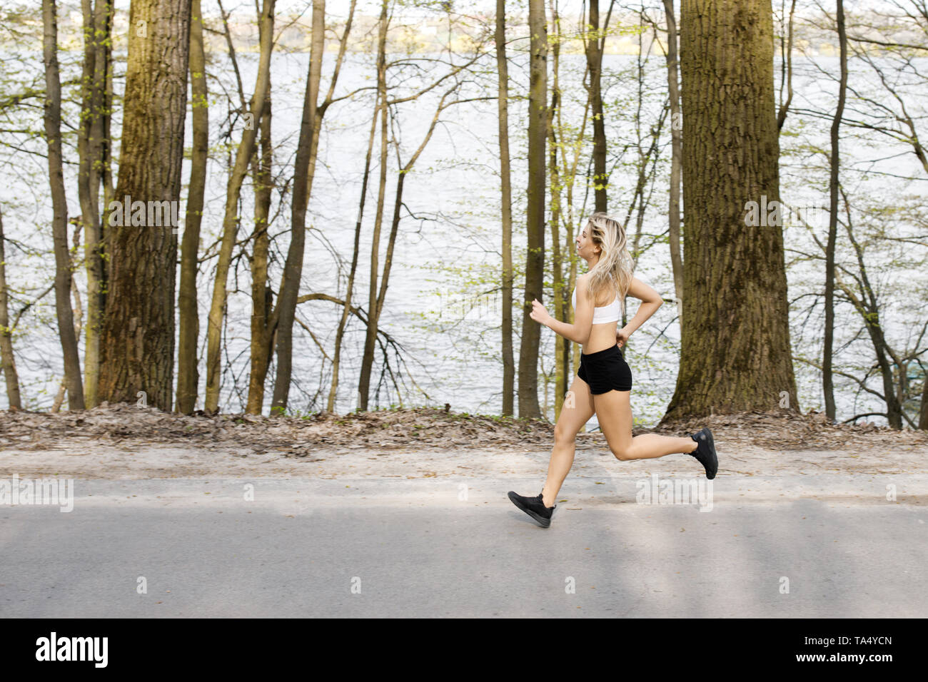 Eine junge, hübsche Mädchen blond läuft draußen in den Wäldern in der Nähe der See und die schöne Landschaft. Sportliche Aktivität. Übung im Freien. Stockfoto