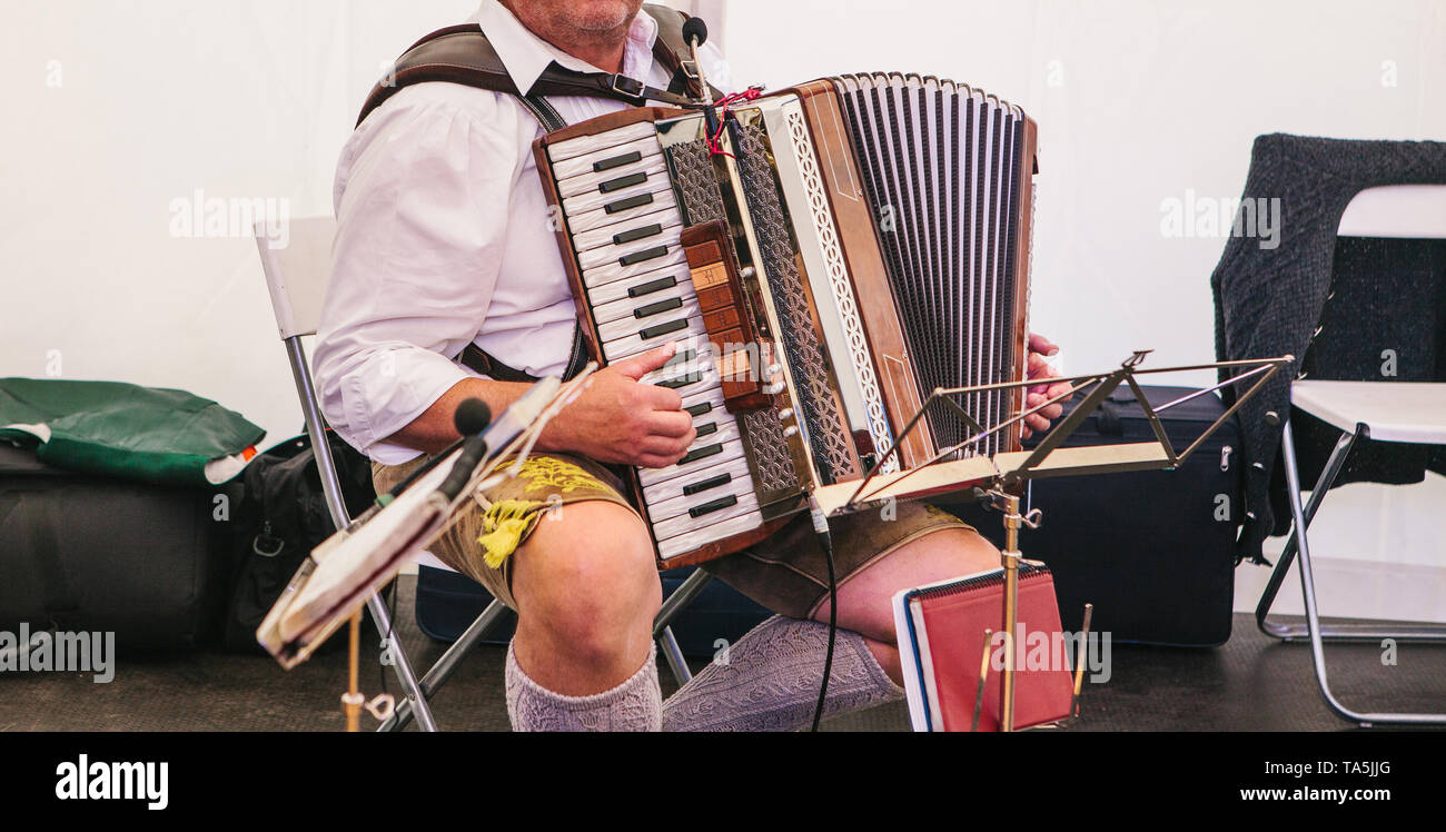 Akkordeonspieler in Traditionelle bayerische Kleidung spielt das Akkordeon auf der Bühne. Der Akkordeonist spielt das Musikinstrument. Stockfoto