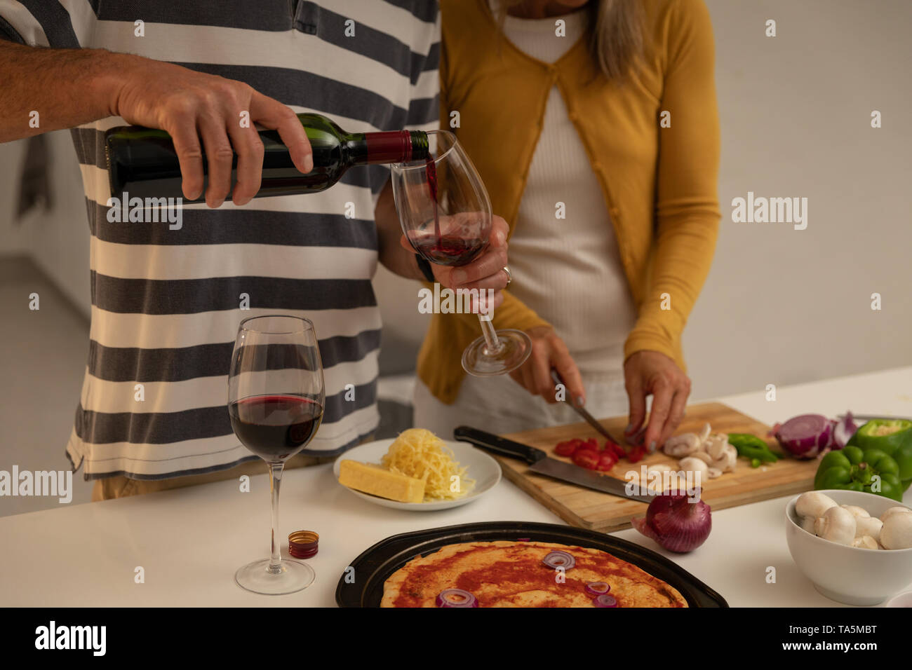 Man gießen Wein im Glas, während Frau Schneiden von Gemüse in der Küche zu Hause. Stockfoto