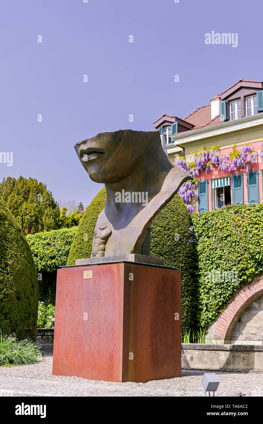Skulptur von einem grossen Kopf im Park des Olympischen Museum der Schweiz.  Frühling Gras und Blumen im Park Stockfotografie - Alamy