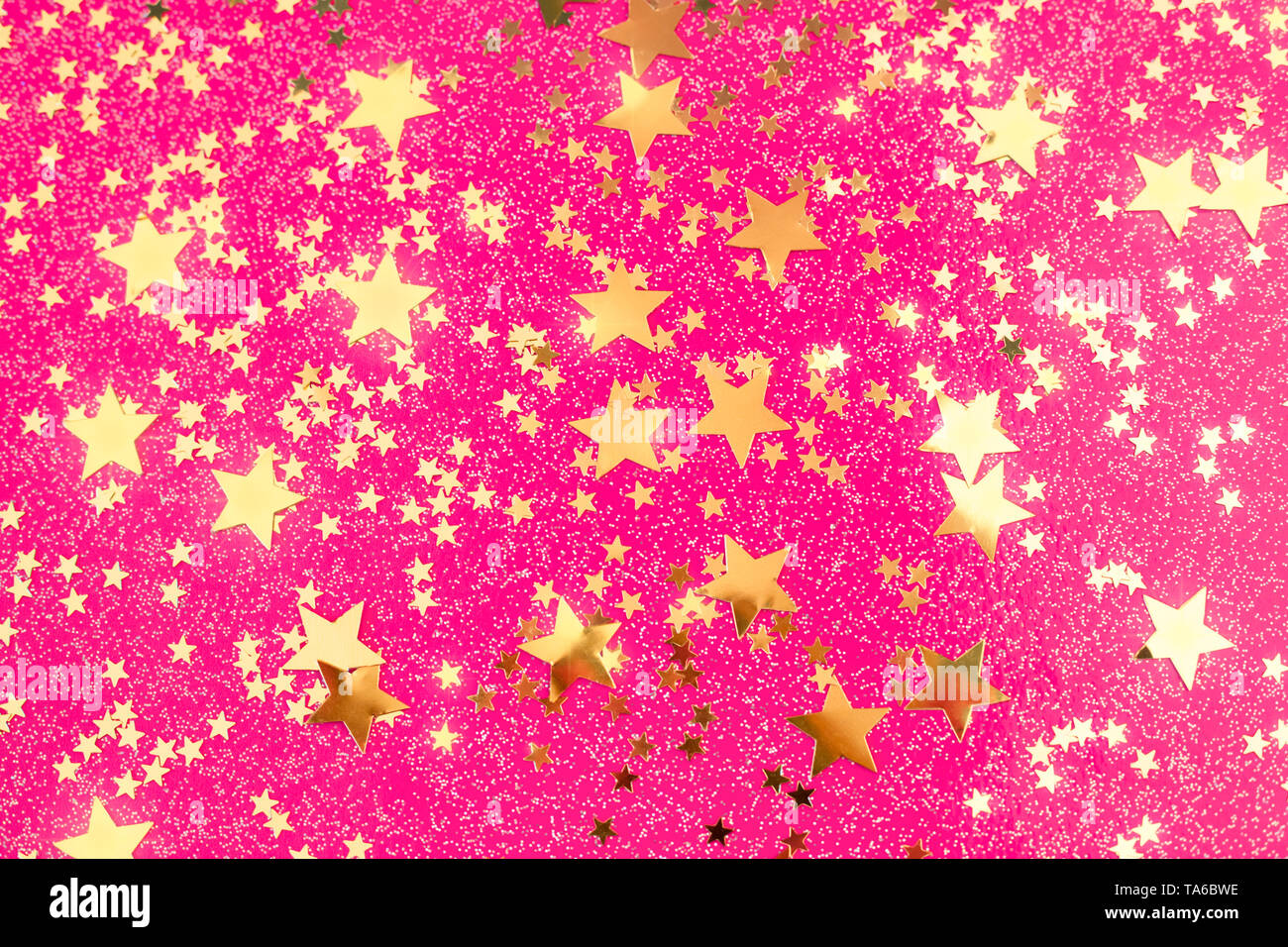 Golden Star Konfetti auf Rosa fuchsia Hintergrund. Festliche Kulisse mit leuchtenden Sternen. Stockfoto