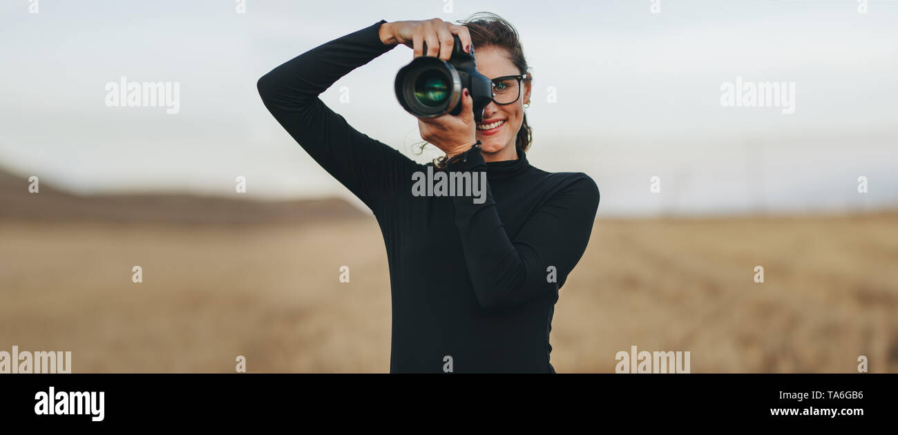 Professionelle Fotografin mit DSLR-Kamera fotografieren im Freien. Junge Frau mit Kamera Bilder aufnehmen. Stockfoto