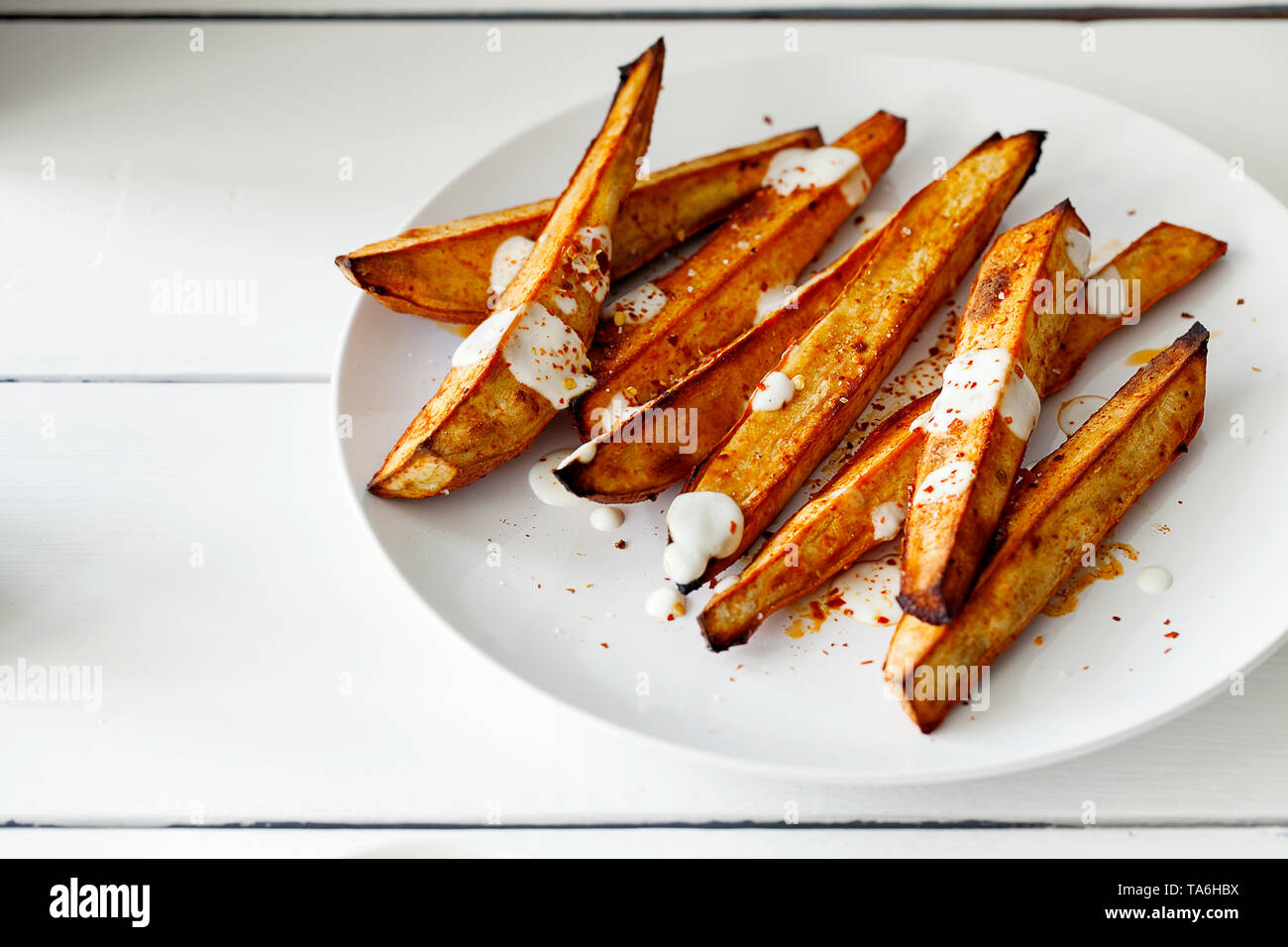 Hausgemachte karamellisierten geröstet geschnitten Süßkartoffeln oder Süßkartoffel mit griechischen Stil Joghurt und zerdrückten roten Pfeffer auf weißem Holz- Hintergrund mit Kopie Raum Stockfoto