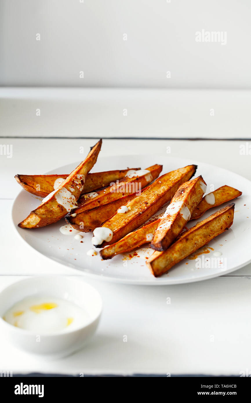 Hausgemachte karamellisierten geröstet geschnitten Süßkartoffeln oder Süßkartoffel mit griechischen Stil Joghurt und zerdrückten roten Pfeffer auf weißem Holz- Hintergrund mit Kopie Raum Stockfoto