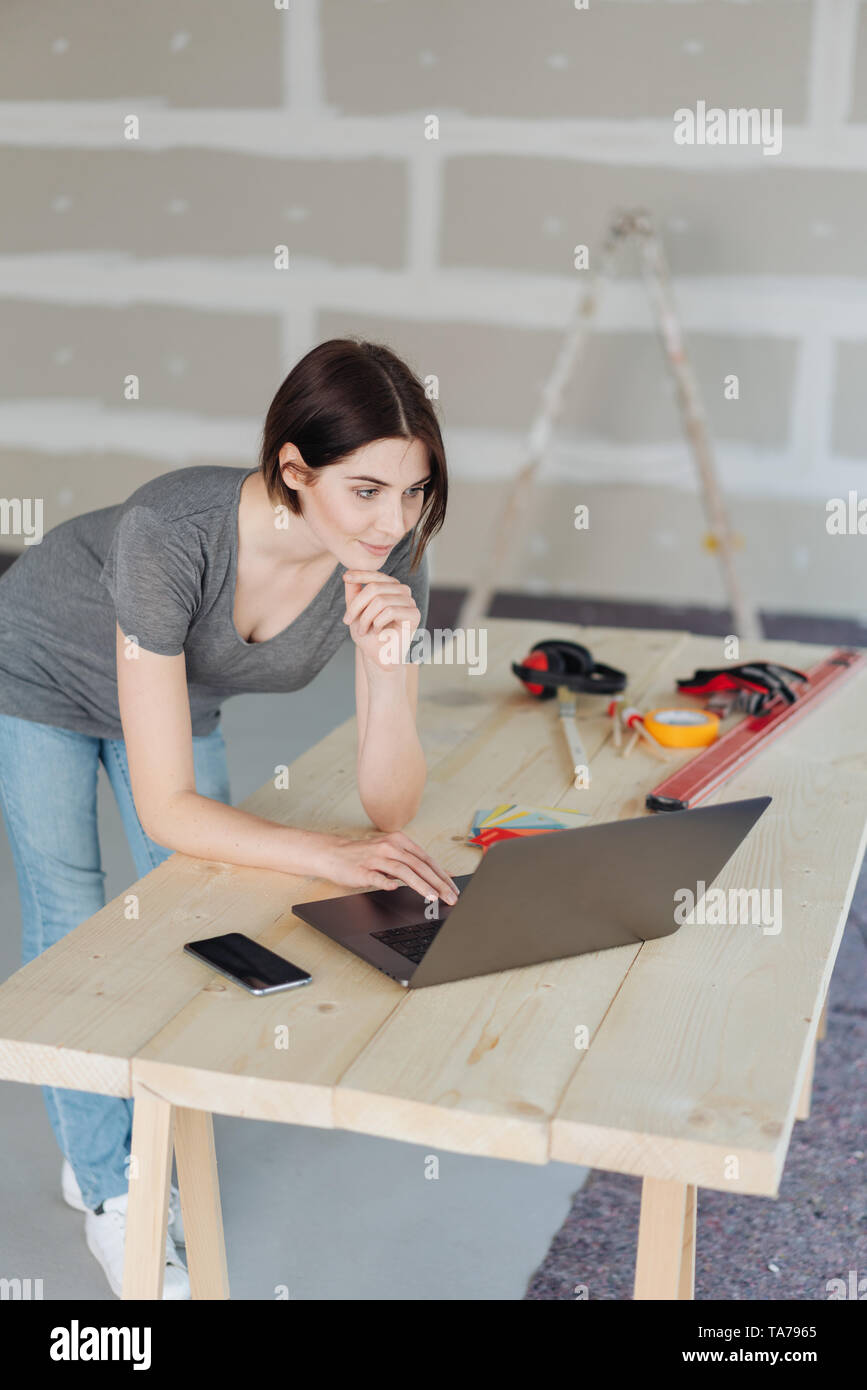Junge Frau, DIY Erneuerungen zu Hause stützte sich auf eine temporäre Arbeit Tabelle arbeitet an einem Laptop Computer durch Tools umgeben Stockfoto