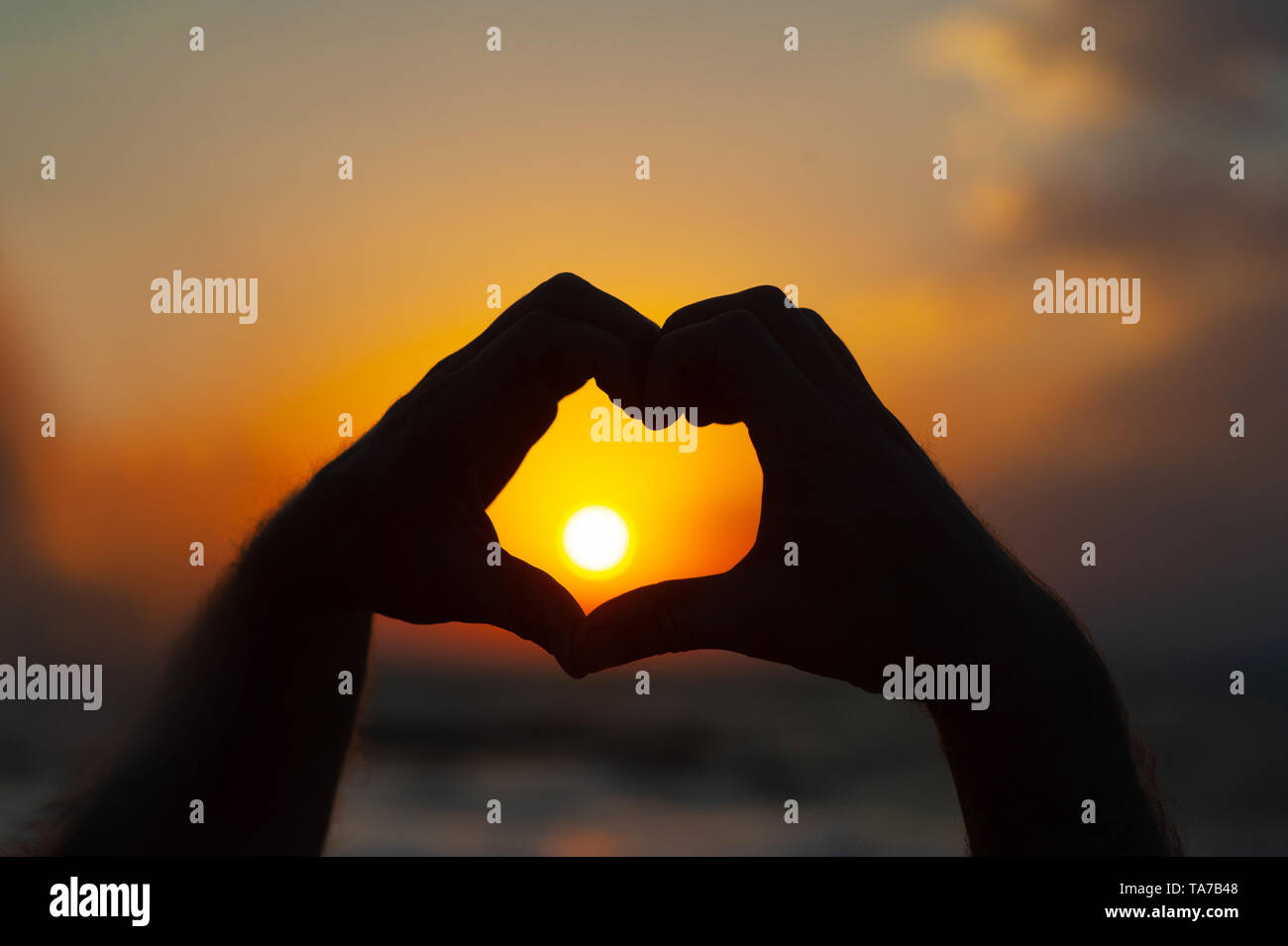 Männliche Hände in Form von Herz gegen den Himmel passieren Sonnenstrahlen. Hände in Form von Liebe Herz Stockfoto