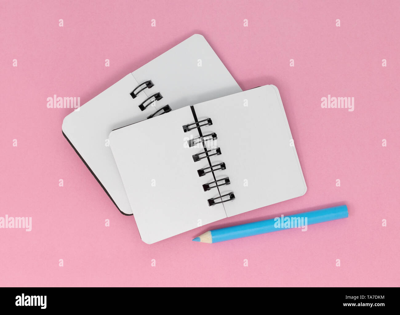 Zwei offene leere Notebooks und einem blauen Bleistift auf einem rosa Hintergrund. Stockfoto