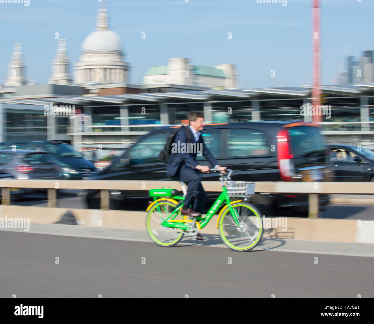 Ein Mann in Anzug, einen elektrischen Teilen bike Lime-E in Bewegungsunschärfe auf Blackfriars Station mit St. Pauls auf Hintergrund Stockfoto