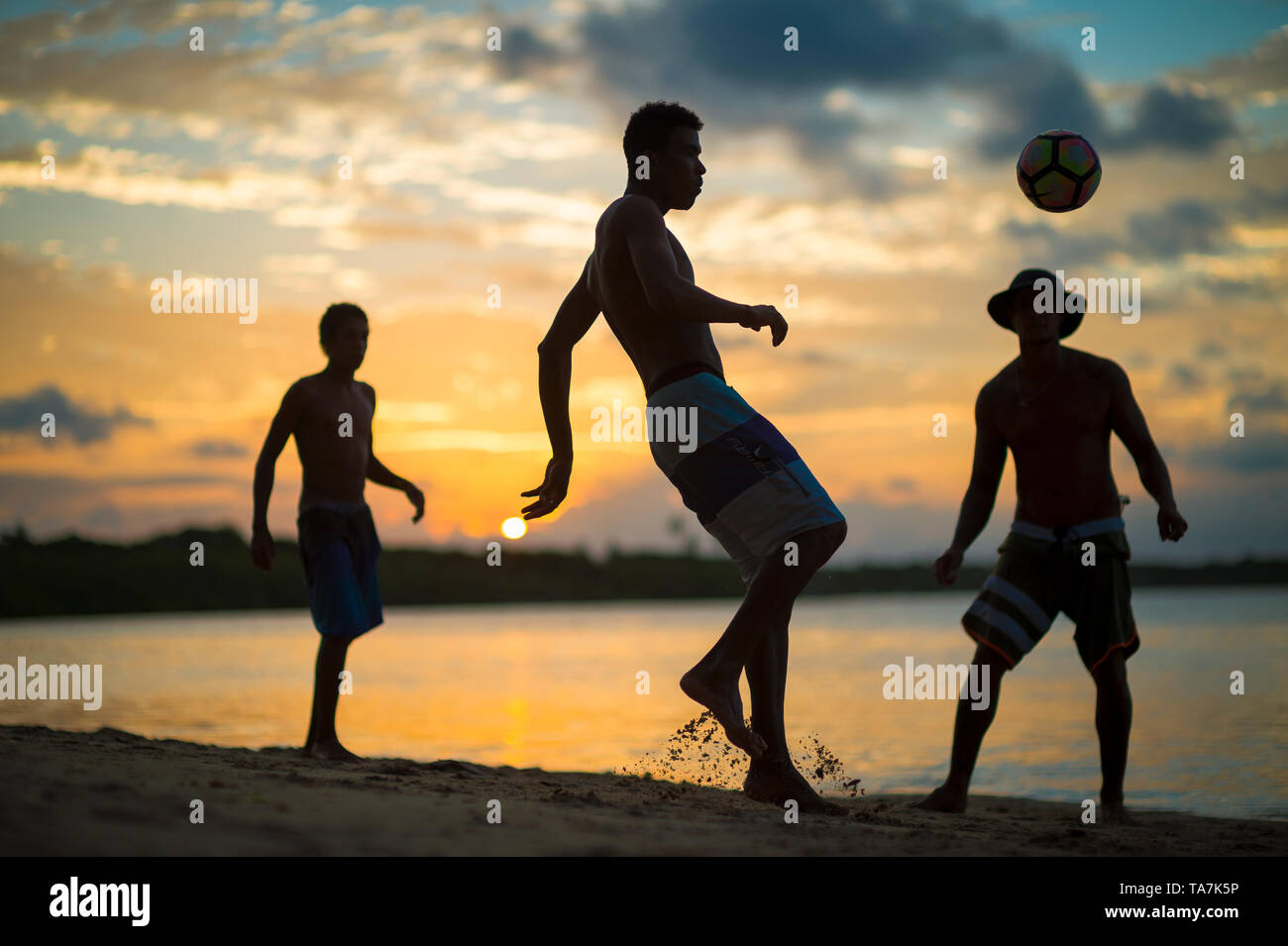CAIRU, Brasilien - Februar, 2018: Junge Männer spielen eine informelle Spiel der Fußball-Keepy Uppy in Silhouette am Ufer eines Sunset Beach. Stockfoto
