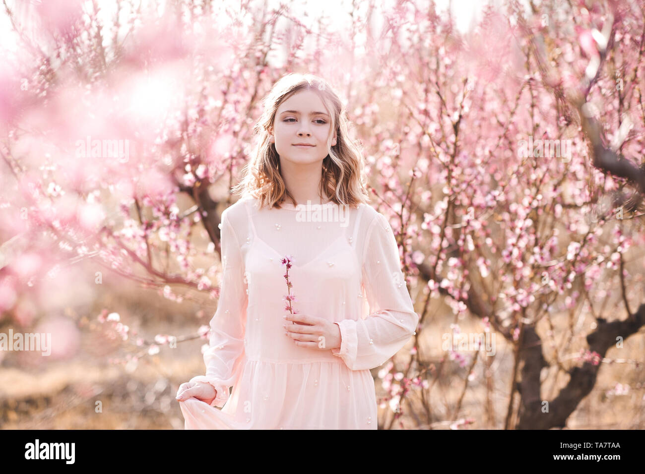 Blonde Mädchen 16-17 Jahre alten Wandern in Peach Orchard. Mit Blick auf die Kamera. Frühling Saison. Stockfoto