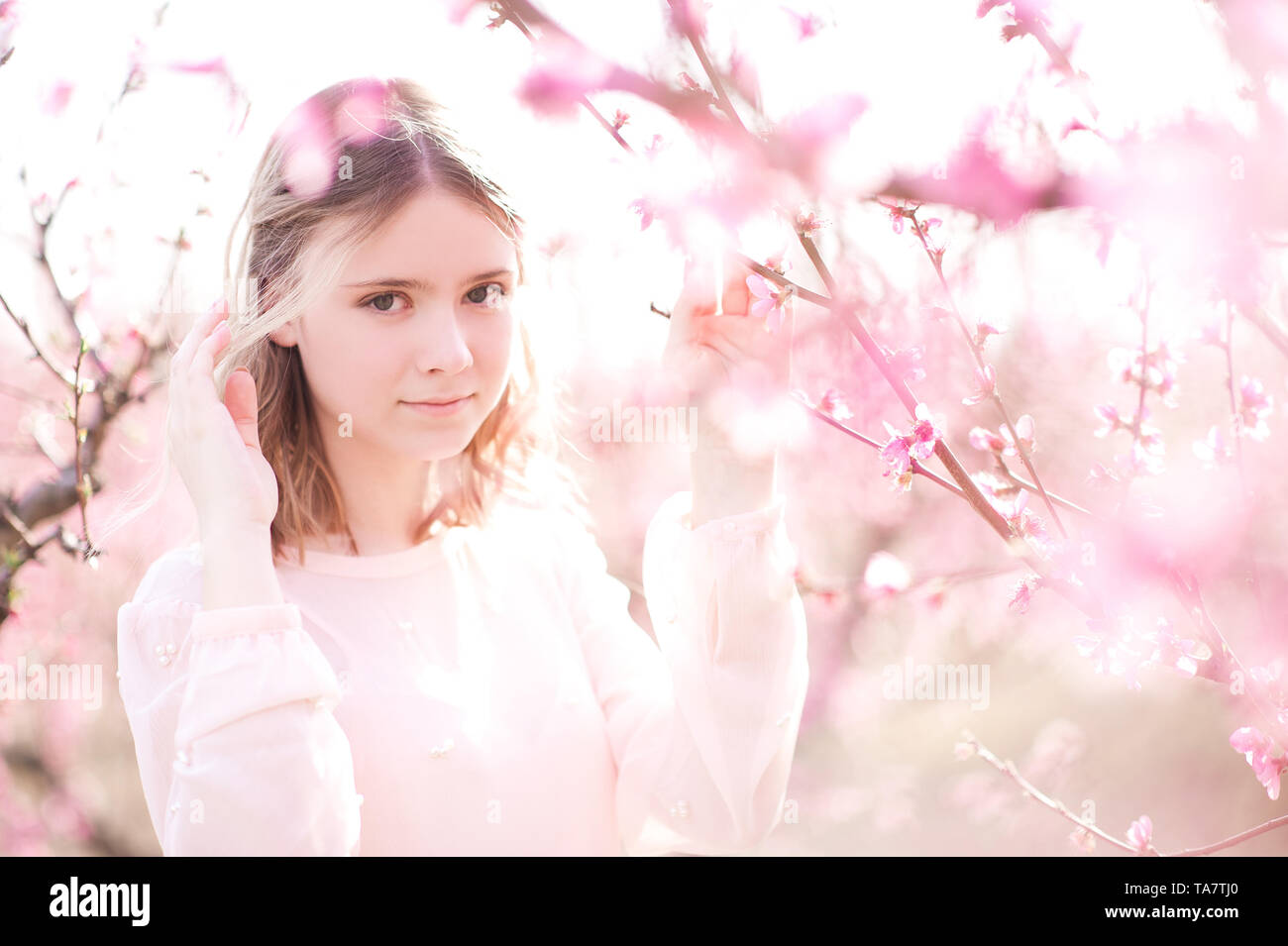 Lächelnde blonde Mädchen 16-17 Jahre alten in pink Peach Blumen closeup draußen posieren. Mit Blick auf die Kamera. Frühling Saison. Stockfoto