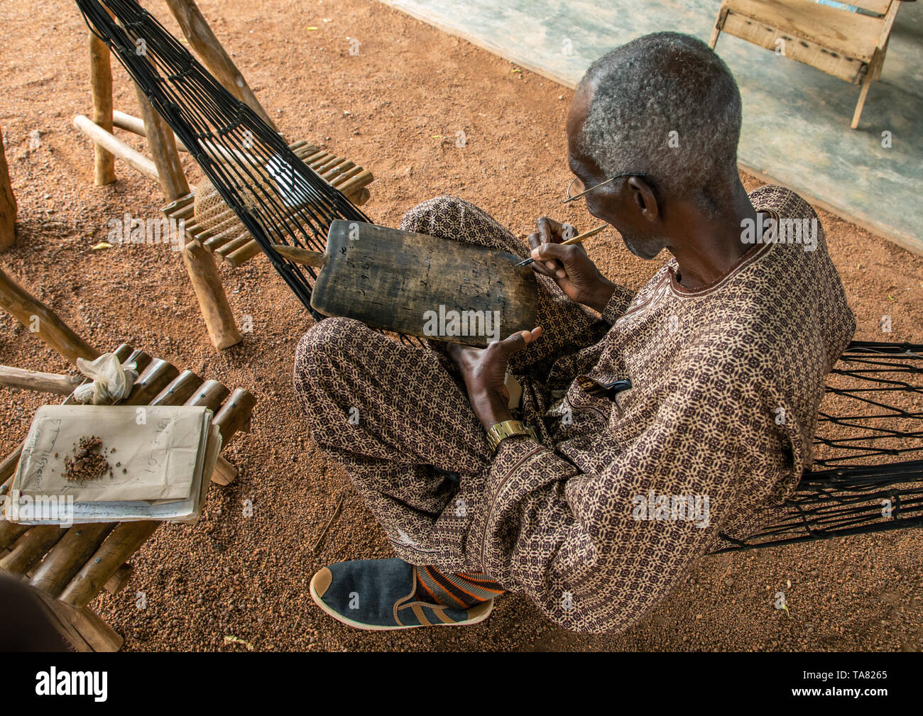 Älterer Mann auf einer Hängematte schreiben Koran auf ein Holzbrett sitzen, Savanes Bezirk, Kouto, Elfenbeinküste Stockfoto