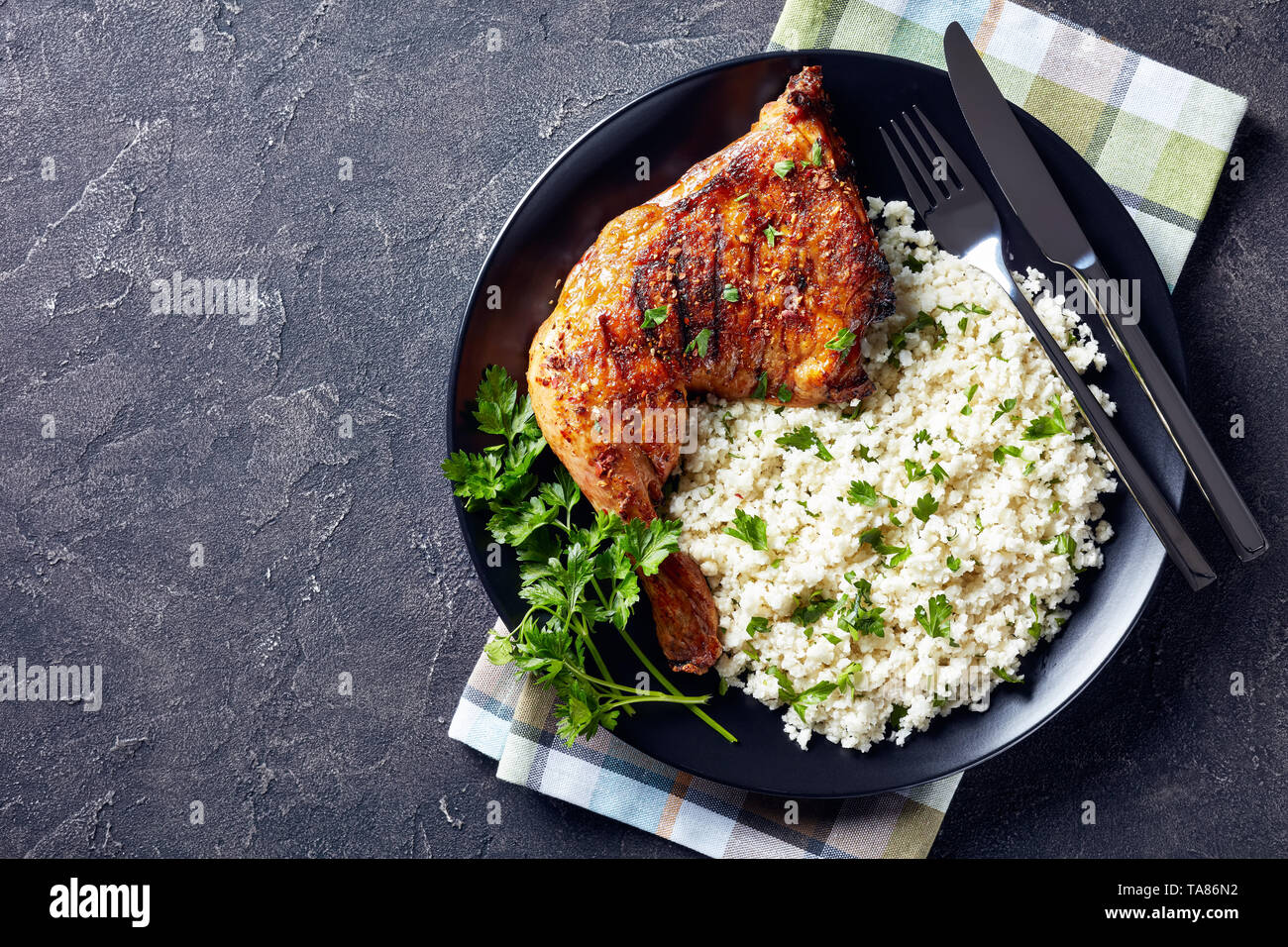 Gegrilltes Hähnchen bein Quartal serviert mit Blumenkohl, Reis oder Couscous auf einer schwarzen Platte auf einer konkreten Tabelle, horizontale Ansicht von oben, flatlay, leer Stockfoto